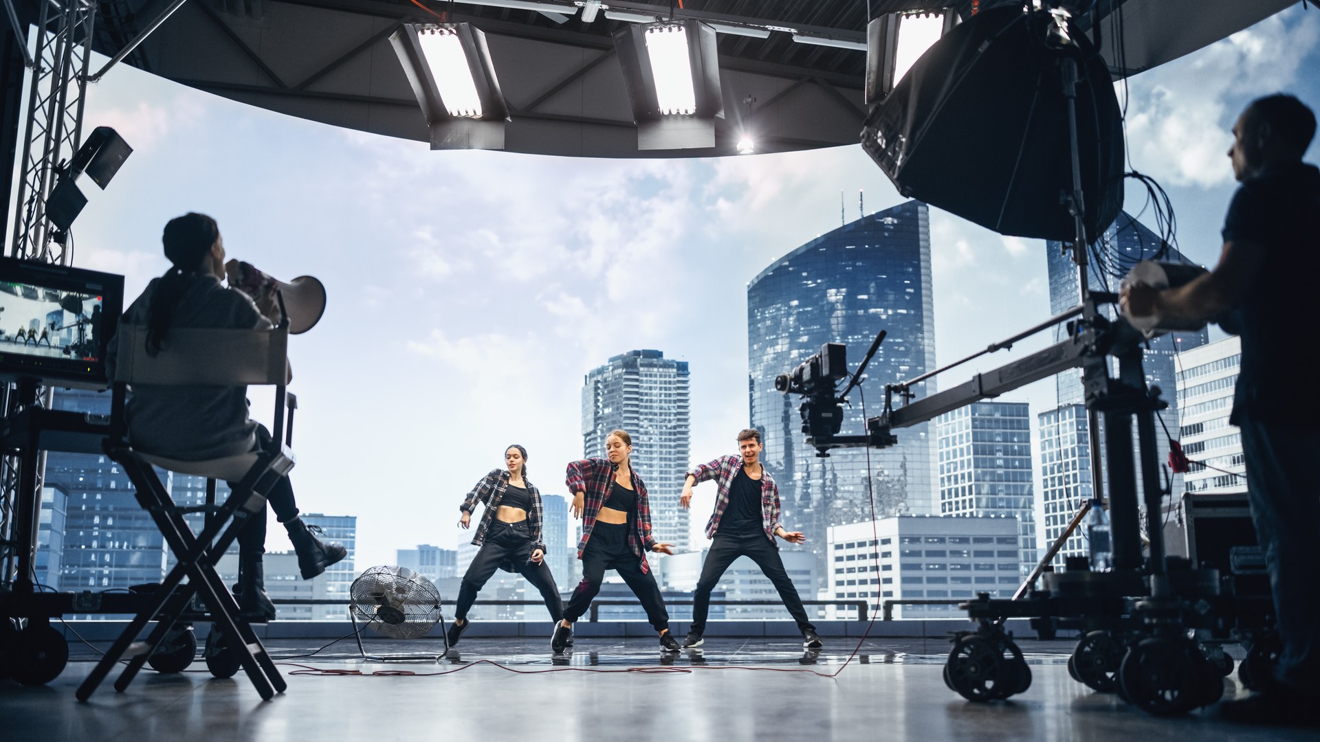 Music Clip Studio Set: Shooting Hip Hop Video Dance Scene with Three Professionals Dancers Performing on Stage with Big Led Screen with Modern City Background. Director and Cameraman in Backstage.